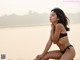 A woman in a black bikini sitting on a beach.